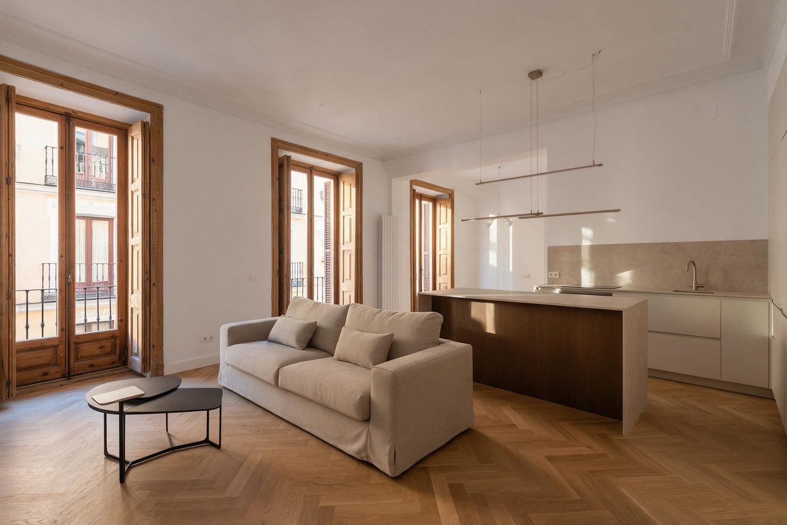 Salón y cocina abierta tras una reforma integral de vivienda en Madrid, con suelo de roble en espiga y balcones restaurados